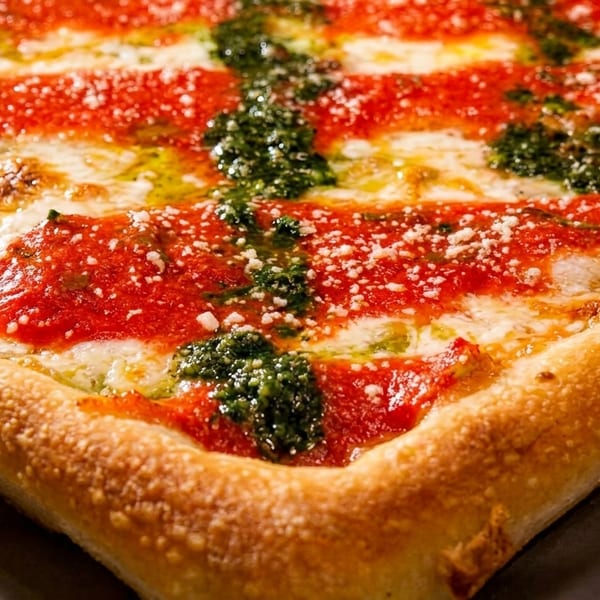 Close-up of a square pizza with red sauce stripes, white cheese, and green pesto swirls.